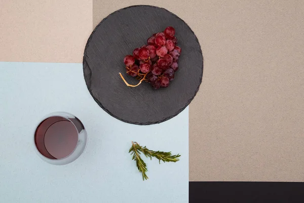 在黑色石板板上的葡萄的顶视图，在五颜六色的背景上，有一杯红酒和迷迭香树枝 — 图库照片