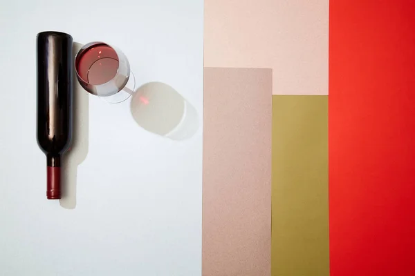 在五颜六色的几何纸背景上，将酒瓶和一杯红酒布局 — 图库照片
