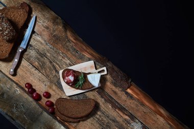 Yukarıdan ahşap kütükler üzerinde sunulan koyu ekmek dilimleri ve peynir ve üzüm çeşitli aperatifler