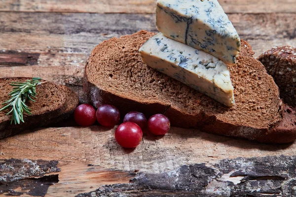 Plasterki chleba zbożowego z aromatycznym serem niebieskim i jagodami winogronowymi na drewnianych desek — Zdjęcie stockowe