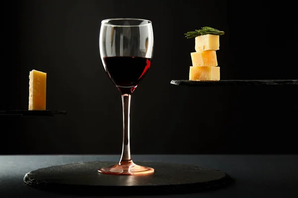 Portie rode wijn en stukjes kaas op een zwarte achtergrond — Stockfoto