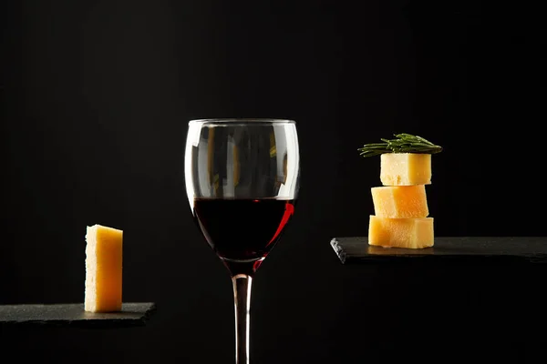 Glass of red wine and pieces of cheese on black background — Stock Photo, Image