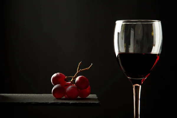 Состав красного вина в стакане рядом с голубым сыром и виноградом на черном фоне . — стоковое фото