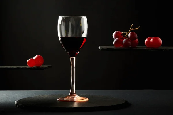 Сладкое красное вино в стакане и свежие ягоды винограда на черном фоне — стоковое фото