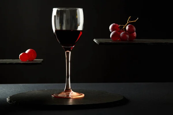 Сладкое красное вино в стакане и свежие ягоды винограда на черном фоне — стоковое фото