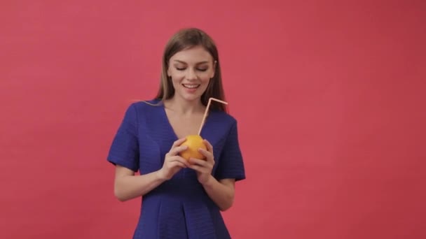 Schönes Mädchen in einem Kleid, das Orangensaft mit einem Cocktail-Strohhalm trinkt und tanzt. Studio, lila Hintergrund — Stockvideo