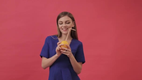 Menina bonita em um vestido beber suco de laranja com uma palha de coquetel e dança. Estúdio, fundo roxo — Vídeo de Stock