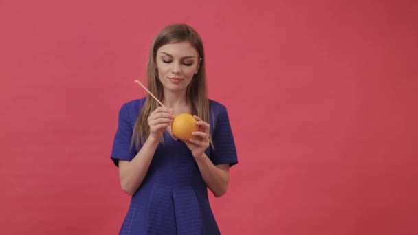 En vacker flicka i en klänning som ansluter hörlurar till en orange och sedan dansar och lyssnar på musik. Studio, lila bakgrund — Stockvideo