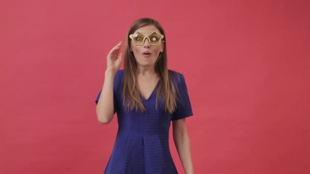 Hermosa chica en un vestido bailando en gafas amarillas en forma de estrella. Estudio, fondo púrpura — Vídeo de stock