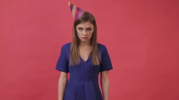 Sad girl in a festive hat, blowing a party whistle. Studio, purple background — Stock Video