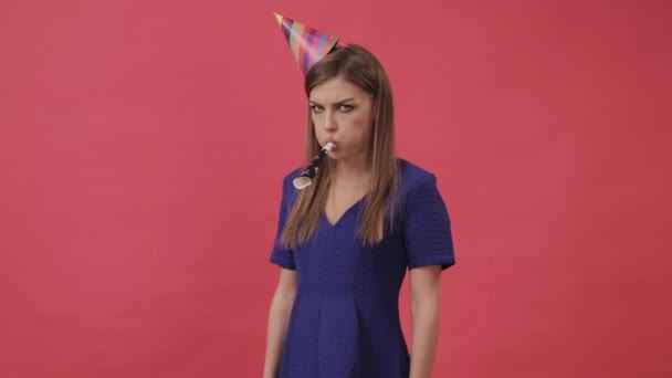 Sad girl in a festive hat, blowing a party whistle. Studio, purple background — Stock Video