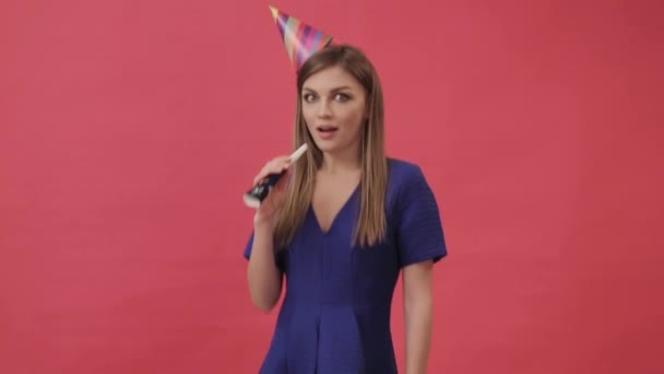 Positive woman in a birthday hat, blowing a party whistle. Studio, purple background — Stock Video
