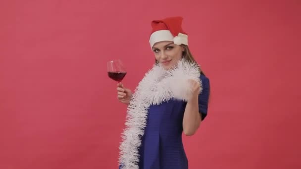 Hermosa chica en ropa de Navidad bailando con una copa de vino en la mano. Estudio, fondo rosa . — Vídeos de Stock