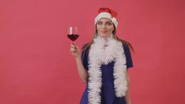 Mooi meisje in kerst kleding dansen met een glas wijn in haar hand. Studio, roze achtergrond. — Stockvideo