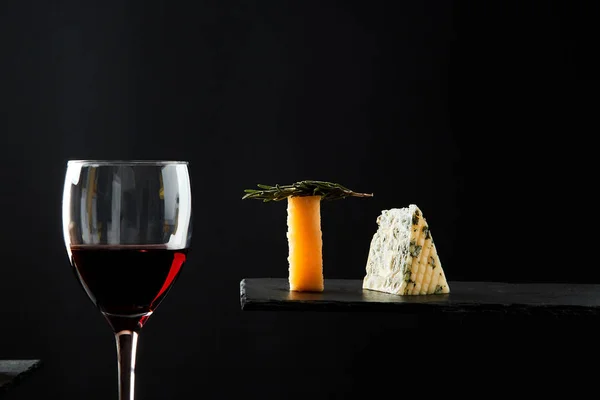 Rode wijn in kristal glas naast stukjes kaas op zwarte achtergrond — Stockfoto