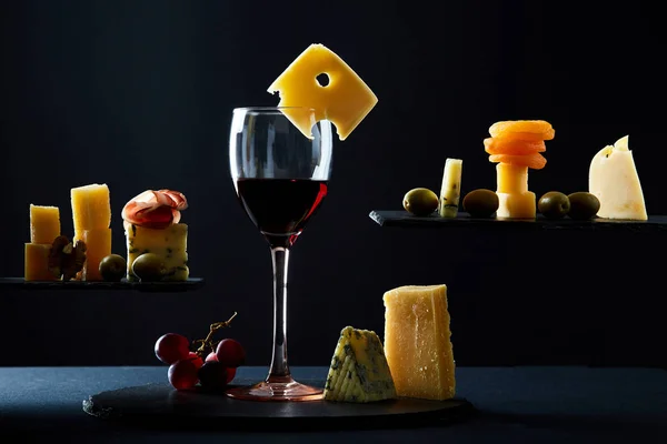 Glas smakelijke rode wijn onder diverse traditionele hapjes op zwarte achtergrond — Stockfoto