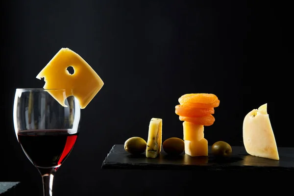 Glas smakelijke rode wijn Next assorti traditionele hapjes op zwarte achtergrond — Stockfoto