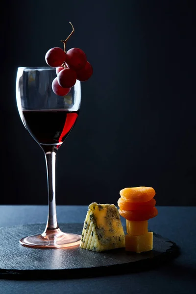 Стакан вкусного красного вина, украшенного кучей винограда на черном фоне — стоковое фото