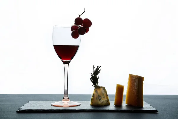 Glass of red wine garnished with grape and pieces of savory cheese — Stock Photo, Image