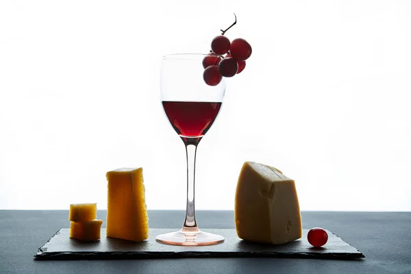 Бокал красного вина, украшенный виноградом и различными видами сыра — стоковое фото