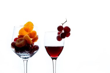 Beyaz arka planda cam ve bir bardak kırmızı şarap kuru kayısı ve üzüm meyveleri