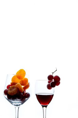 Beyaz arka planda cam ve bir bardak kırmızı şarap kuru kayısı ve üzüm meyveleri