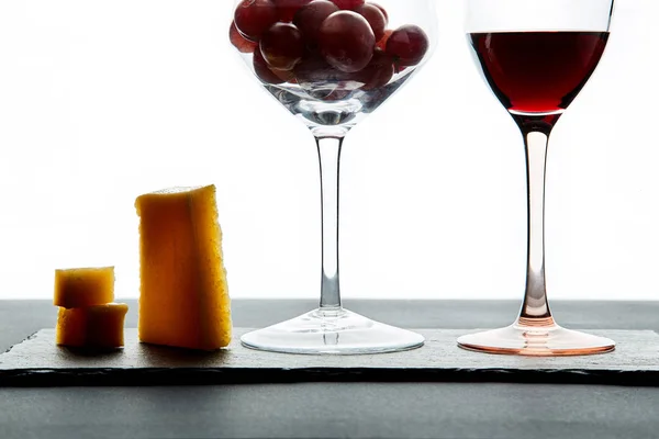 Несколько кусочков сыра и помидоров черри рядом с бокалом красного вина, наполненного виноградом на белом фоне — стоковое фото