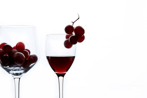 Red grape and wine in crystal glasses on white background