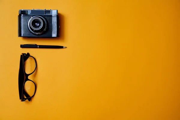 Bloglama, blog ve blogger veya sosyal medya kavramı: gözlük, fotoğraf makinesi ve sarı arka plan üzerinde bir kalem. Düz yatıyordu — Stok fotoğraf