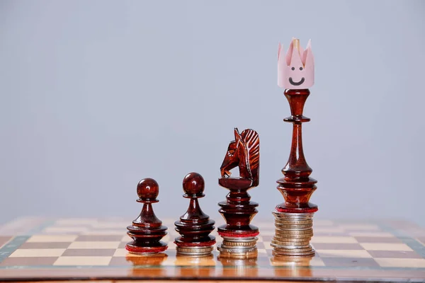 Jogo de xadrez, liderança e conceito de competição. Vencedor e líder. Rei xadrez numa coroa de papel. Conceito de investimento — Fotografia de Stock