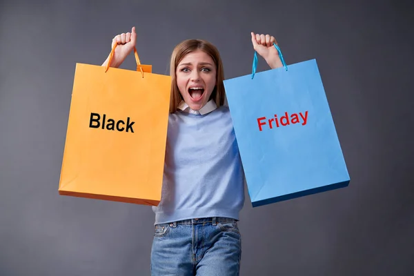 Emotional girl with colored bags standing on a gray background. Sale, shopping, discount concept. Black friday.