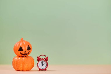 Sonbahar tatili için plastik süsleme. Kırmızı küçük saat. Turuncu balkabağı. Cadılar Bayramı konsepti Uzayı kopyala Yeşil arkaplan