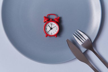 Yemek vakti geldi. Çatal ve bıçakla dolu boş bir masada kırmızı alarmlı saatin üst görüntüsü. Gri arkaplanda izole