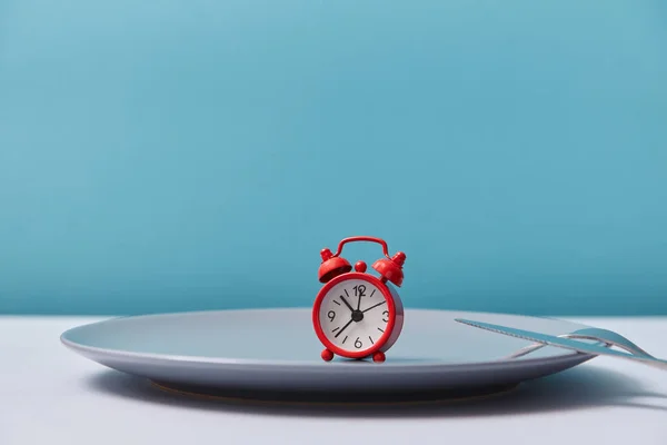 Çatal ve bıçakla gri boş tabakta kırmızı çalar saat. Yemek zamanı. Şenlikli yemek. Kutlama kavramı, kopyalama alanı