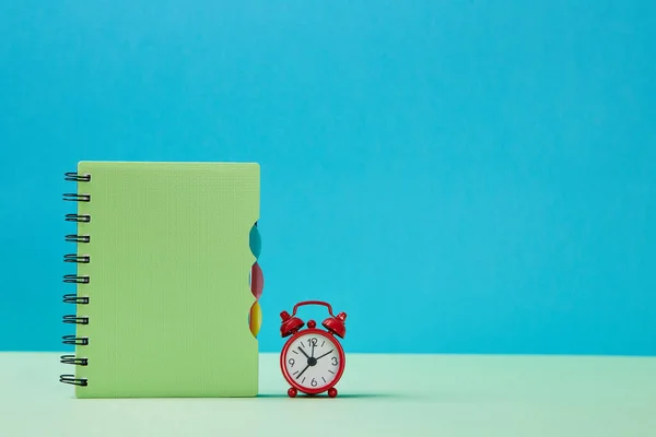 Back to school. Time to study. New school year concept. Notebook and red alarm clock on blue background, copy space — Stock Photo, Image