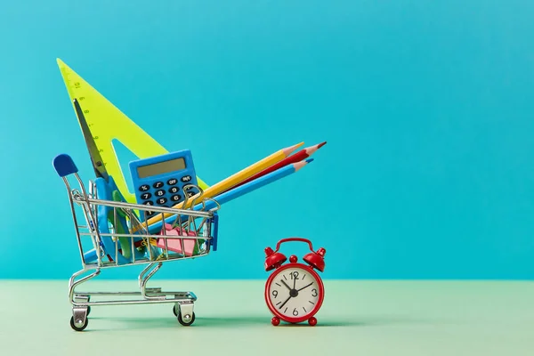 Bienvenido de nuevo a la escuela fondo de venta. Compras escolares. Carro con útiles escolares y despertador. Tiempo para estudiar —  Fotos de Stock