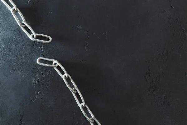 Broken metal chain isolated on black textured background, copy space. Top view of torned up chain. Freedom concept
