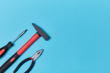 Onarım ve yenileme. İşçi bayramı konsepti. İşçi günü. Mavi üzerine izole edilmiş tornavida, çekiç ve pense üst görünümü