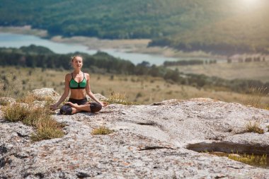 Lotus pozisyonunda bir kadın. Kadın, temiz hava üzerine meditasyon yapıyor. Spor, spor ya da sağlıklı yaşam tarzı konsepti. Yeşil çayırlar.