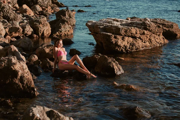 Lány a tengeren. Napozás. Tengerparti nap és napozás. Rózsaszín bikinis hölgy. Éles sziklák és óceánra néző, másolás tér — Stock Fotó