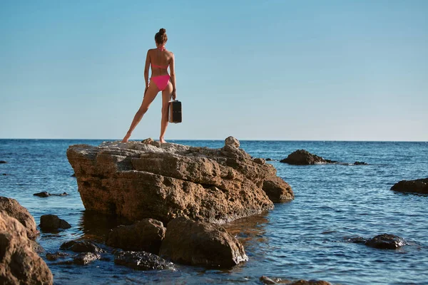 Ideje utazni. Nyári vakáció és vándorlás. Egy hölgy áll a sziklán bőrönddel. Tengerpart és tengerpart. Fénymásolási hely — Stock Fotó