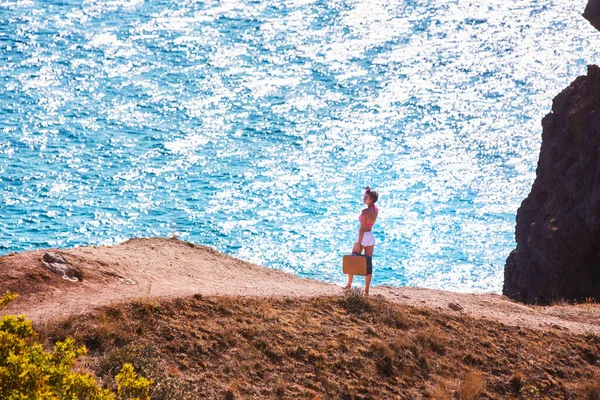 Καλοκαίρι και τουρισμός. Γυναίκα σε ορεινό δρόμο με vintage βαλίτσα. Κρυστάλλινο νερό. Παρθένα φύση. Διακοπές στην παραλία — Φωτογραφία Αρχείου