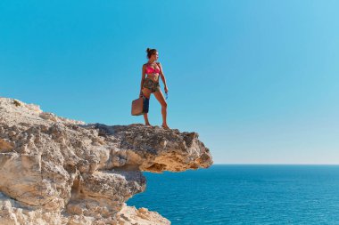 Bavul ve gözlüklü plaj elbiseli kadın. Seyahat zamanı. Yaz tatili. Seyahat arzusu. Uçurumdan okyanus manzarası