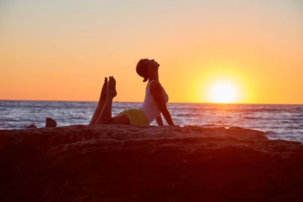 Puesta de sol sobre el océano. Mujer estirándose sobre roca. Estilo de vida activo y deporte. Concepto de tiempo de yoga y pilates, espacio de copia — Foto de Stock