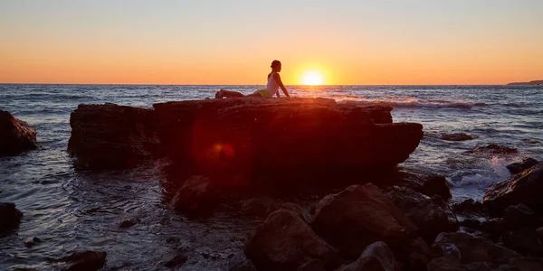 Γυναίκα που τεντώνεται πάνω σε βράχο. Ενεργός τρόπος ζωής και αθλητισμού. Ηλιοβασίλεμα πάνω από ωκεανό. Yoga time and pilates concept, αντιγραφή χώρου — Φωτογραφία Αρχείου