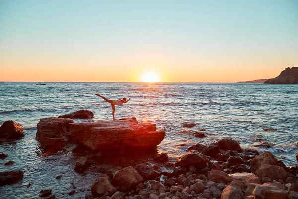 Γυναίκα στέκεται σε θέση γιόγκα. Όμορφο ηλιοβασίλεμα πάνω από τον ωκεανό. Τεντώνοντας και πιλάτες σε φρέσκο αέρα έννοια, αντιγραφή χώρου — Φωτογραφία Αρχείου
