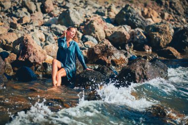 Taş üstünde oturan güzel bir kadın. Kristal temiz deniz suyu. Yaz tatili dinlenme. Meditasyon ve rahatlama konsepti, boşluğu kopyala.