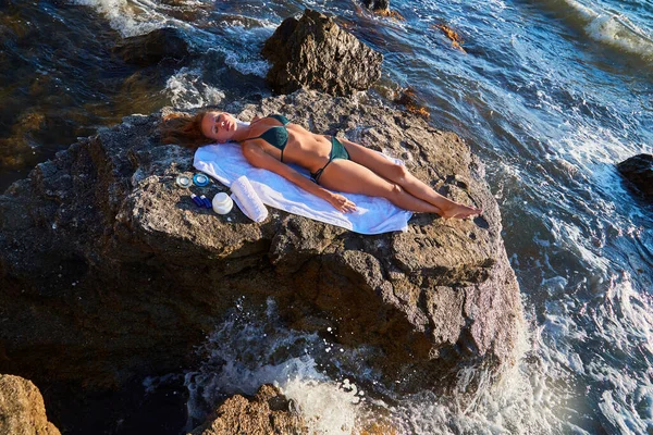 Frau sonnt sich auf Felsen. Felsige Küste und kristallklares Meerwasser. Beauty-Produkte für die Wellness-Behandlung. Entspannungskonzept — Stockfoto