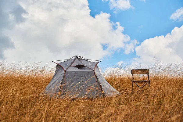 Tienda gris y silla en hierba seca. Prado vacío para descansar. Aire fresco y nueva aventura. Naturaleza virgen y concepto de camping — Foto de Stock