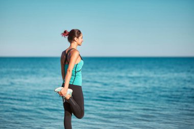 Bacakları kaldıran ve vücudu esneten biri. Güzel bir deniz manzarası ve açık hava eğitimi. Spor ve aktif yaşam tarzı fikri, kopyalama alanı